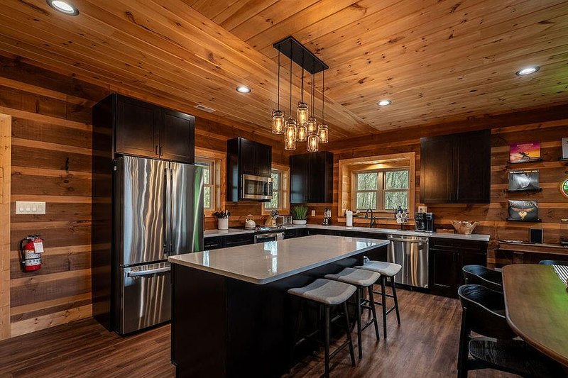 Kitchen island with timber counter stools and low pendants against dark cabinetry